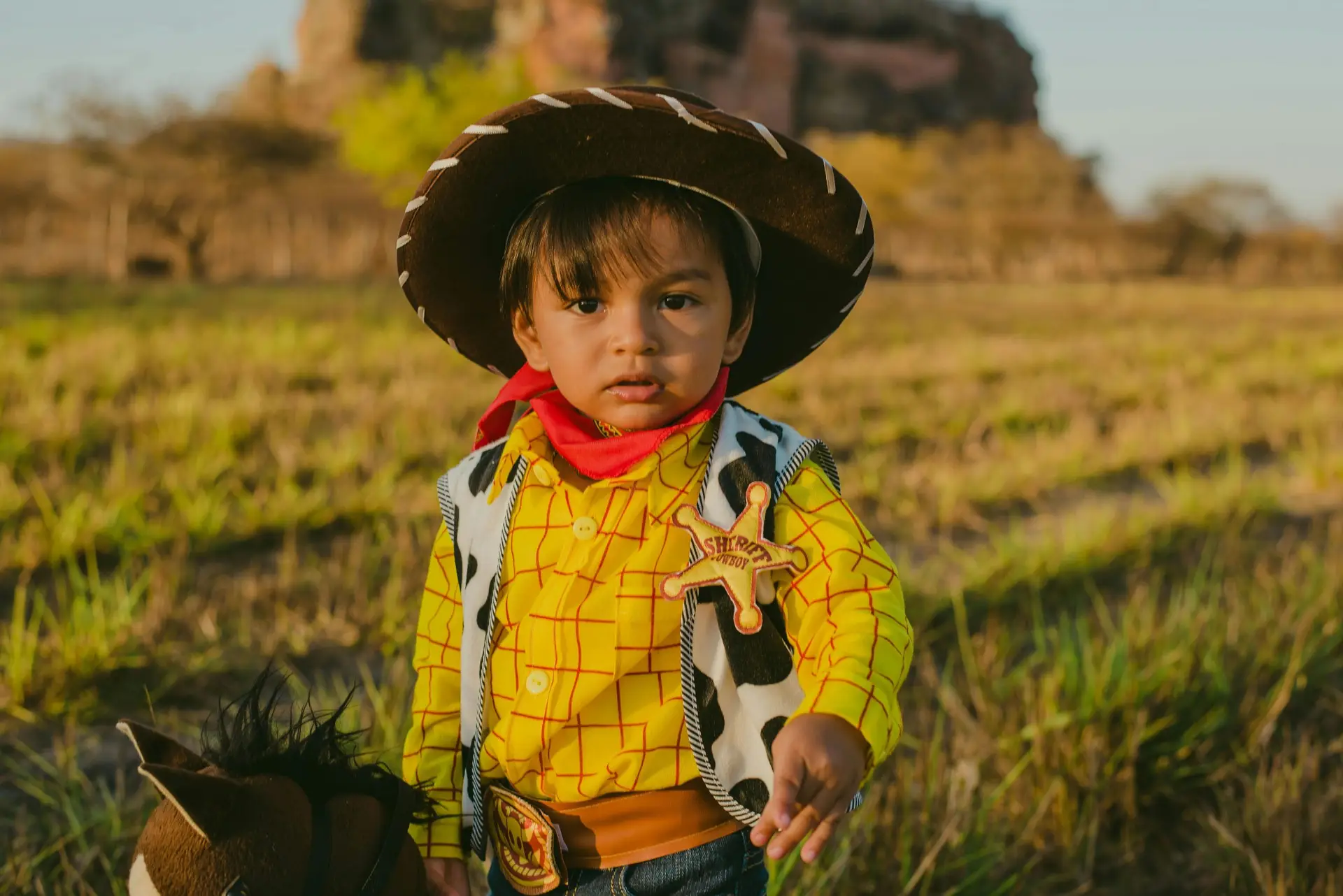 Young child dressed as a cowboy in a field, capturing the playful spirit of a Western-themed photoshoot.