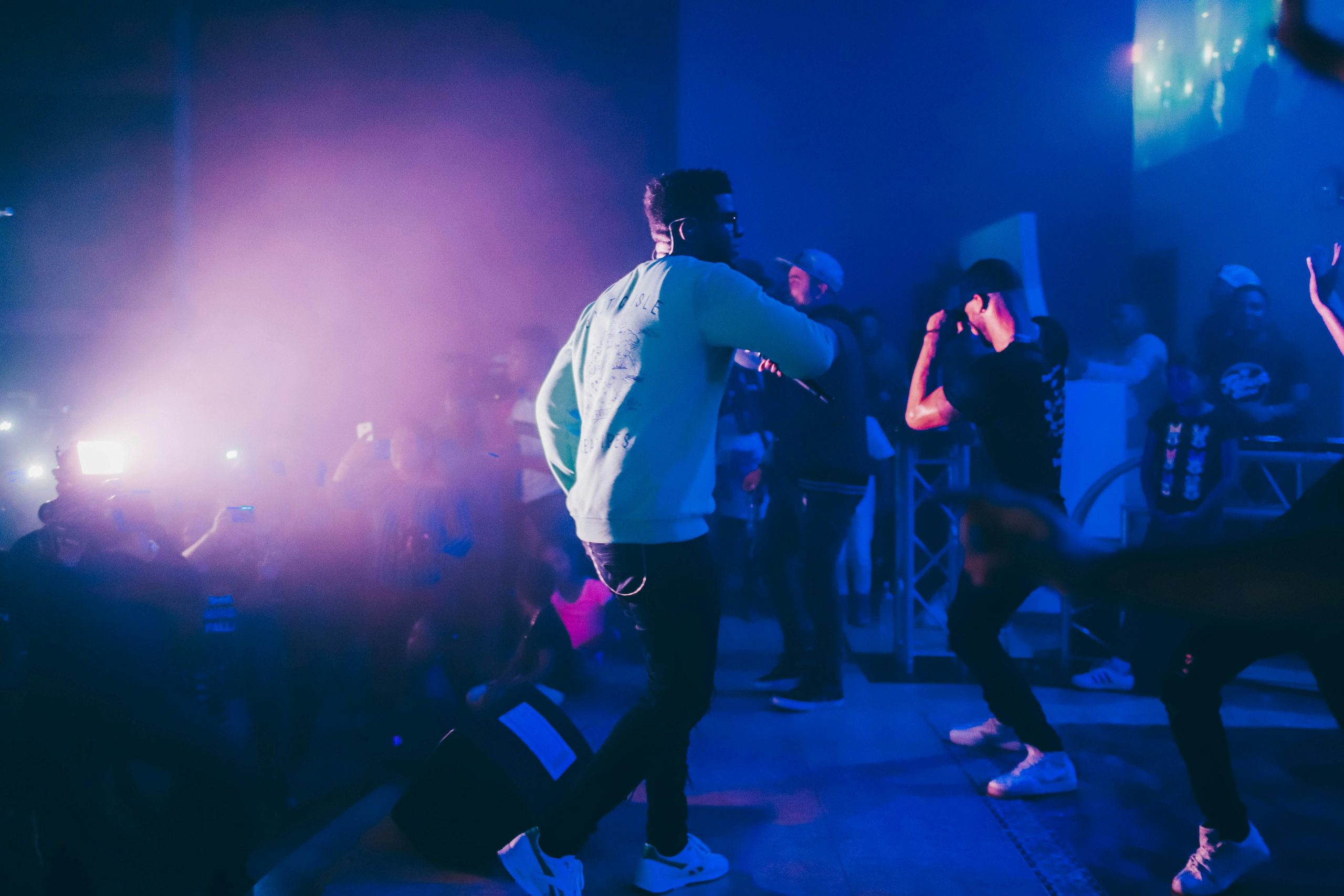 Dynamic live performance featuring a rapper on stage in a vibrant nightclub setting with an enthusiastic crowd.