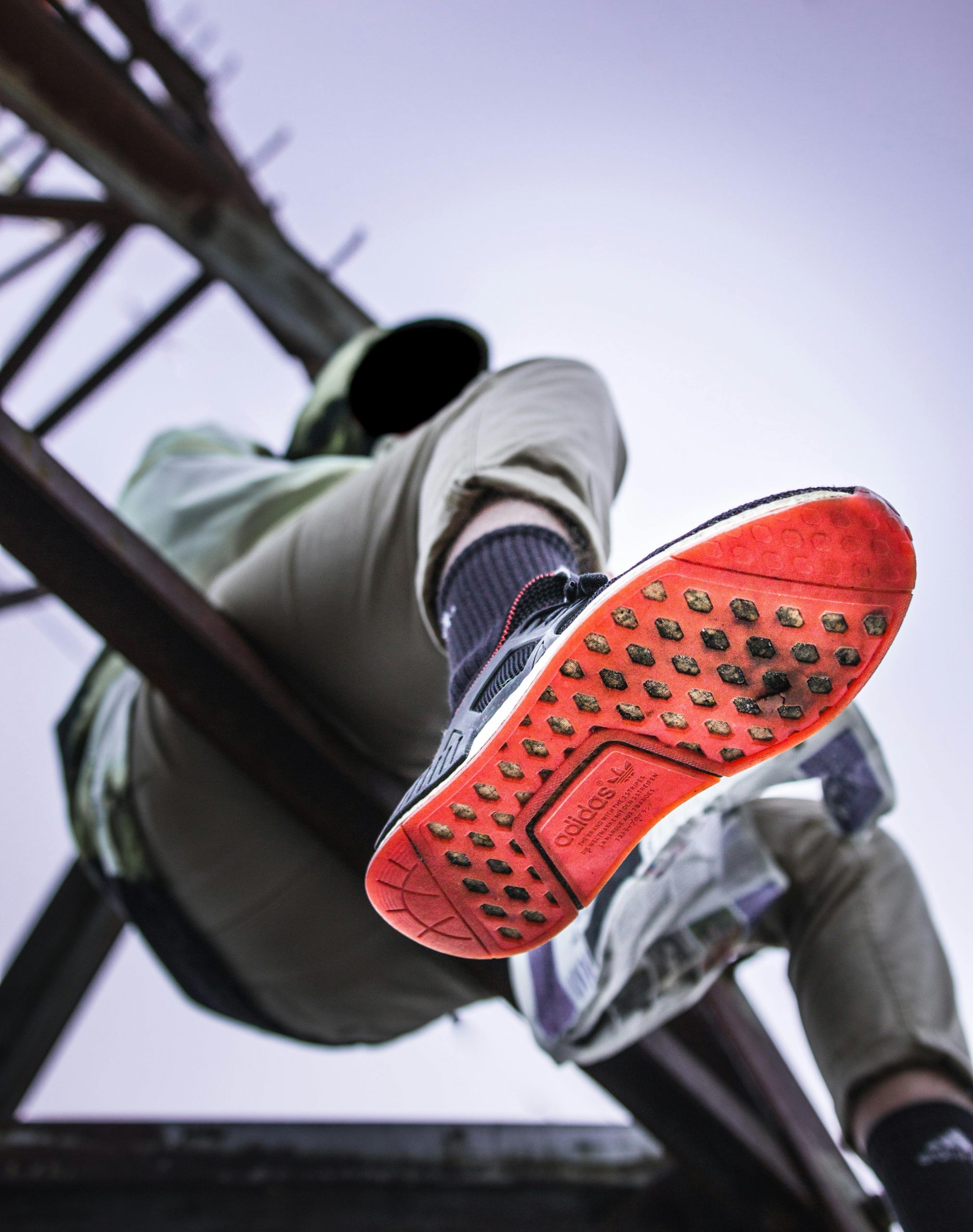 Low-angle view of a person sitting outdoors in Adidas sneakers on a structure.