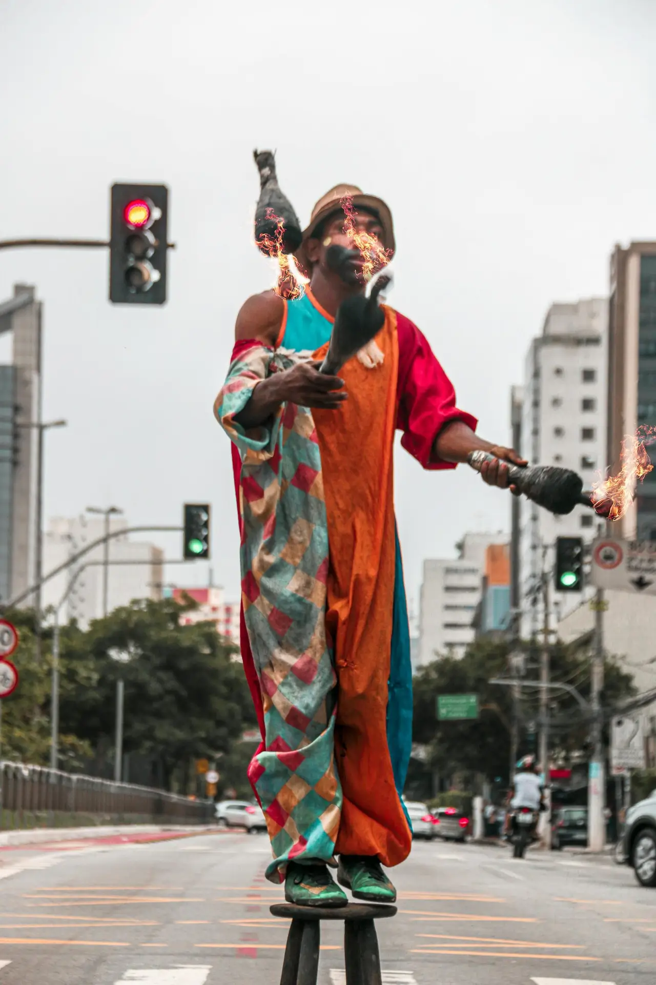 Colorful street performer juggling fire on stilts in a busy urban setting.