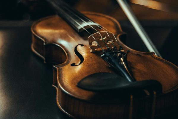 A close-up of a violin resting on a leather chair with a bow, in moody lighting.