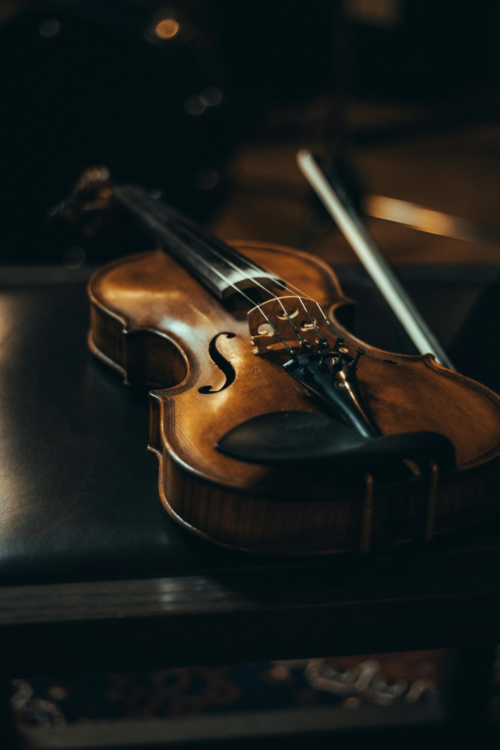 A close-up of a violin resting on a leather chair with a bow, in moody lighting.