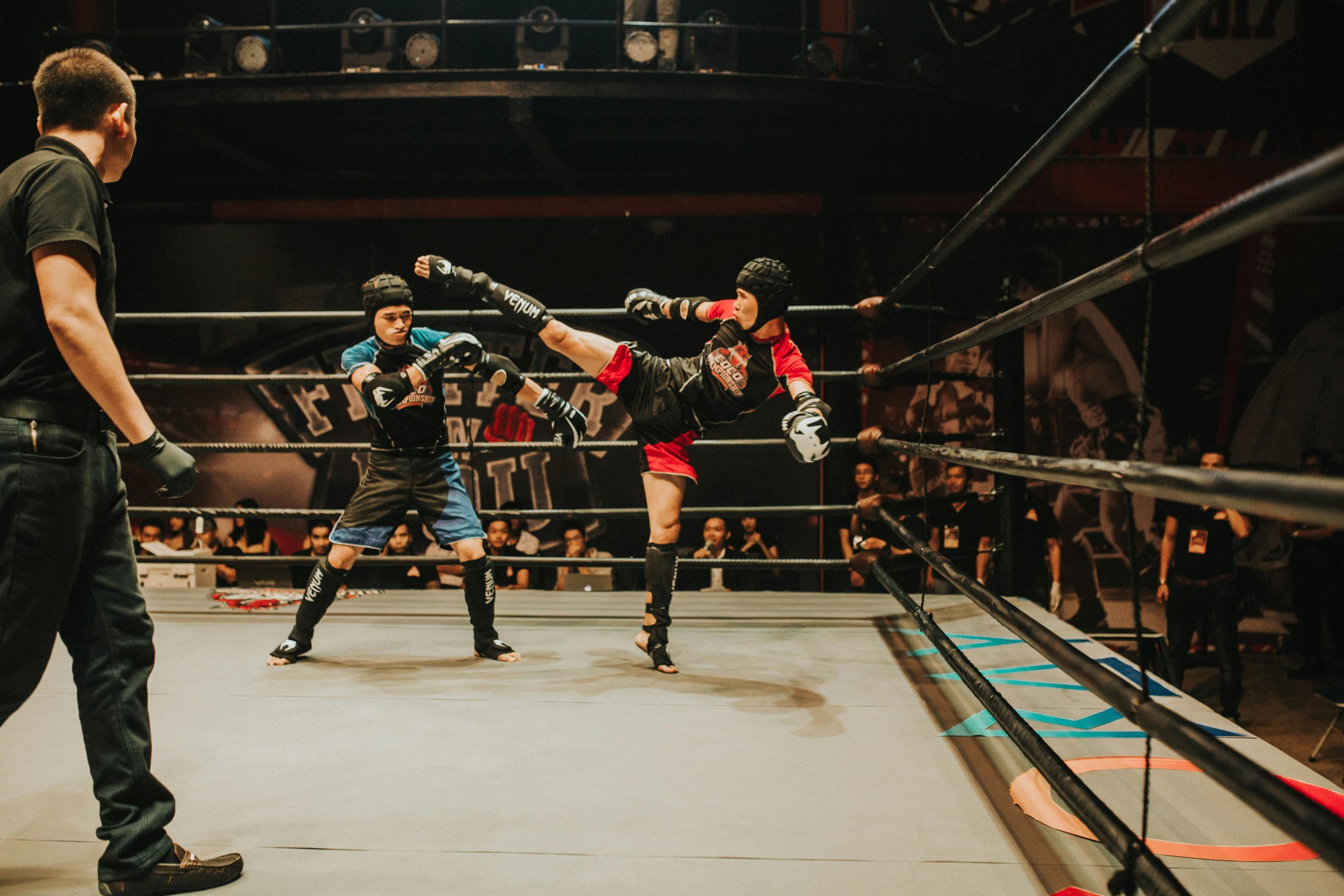 Intense kickboxing match with fighters in action inside a crowded indoor arena.