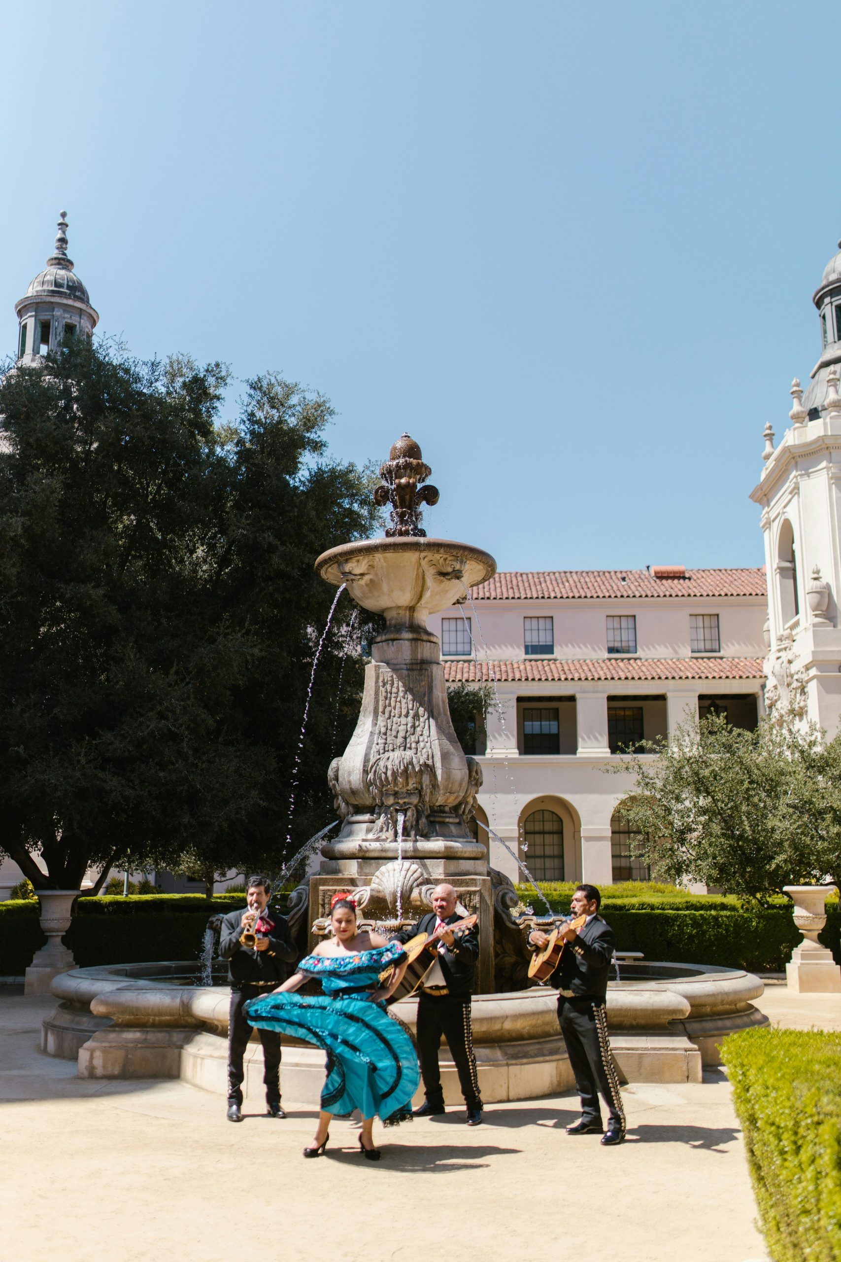 Traditional Mexican performers in vibrant attire around a historic fountain.