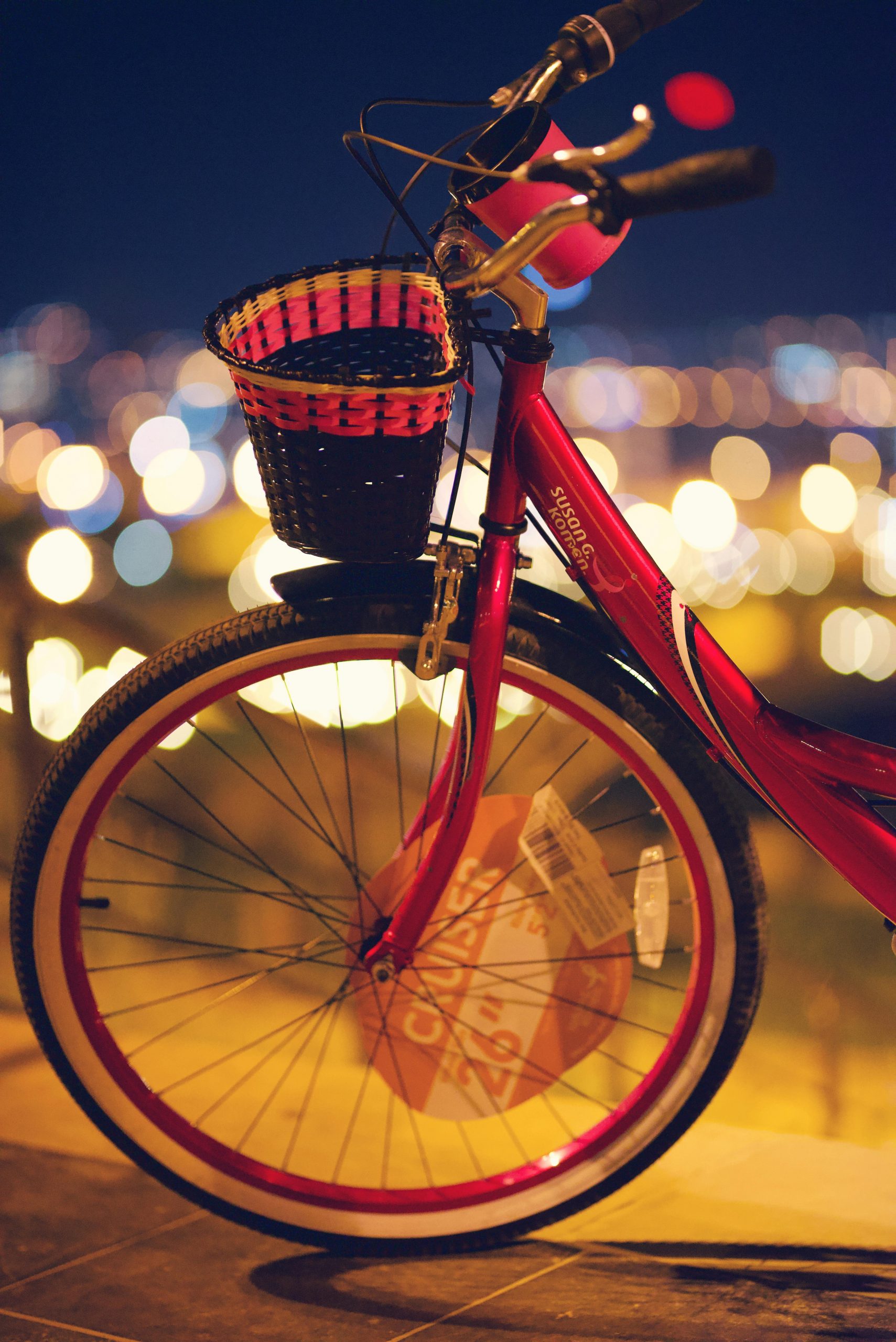 Red bicycle with a basket against blurred city lights at night, showcasing vibrant urban lifestyle.