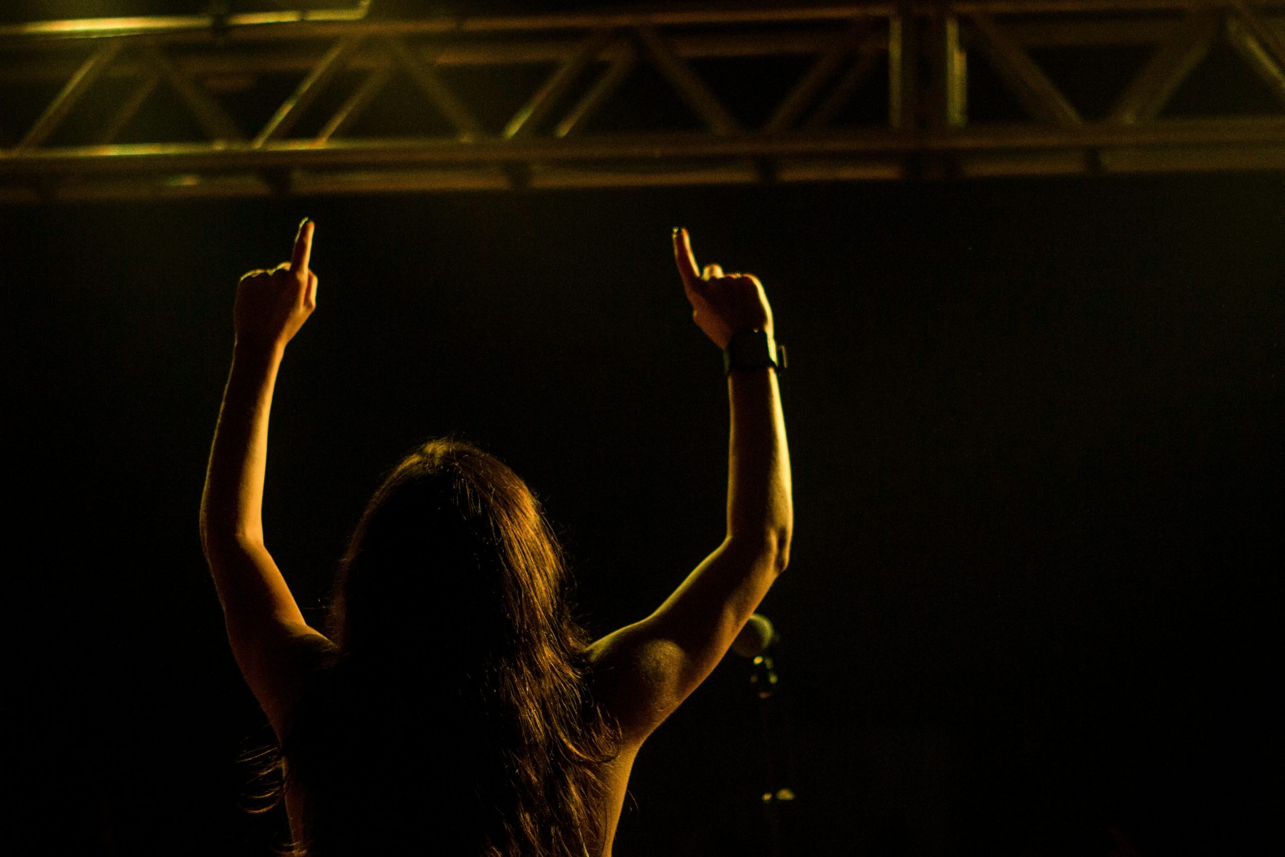 Backlit woman performing on stage, raising arms in front of audience, capturing a lively concert scene.