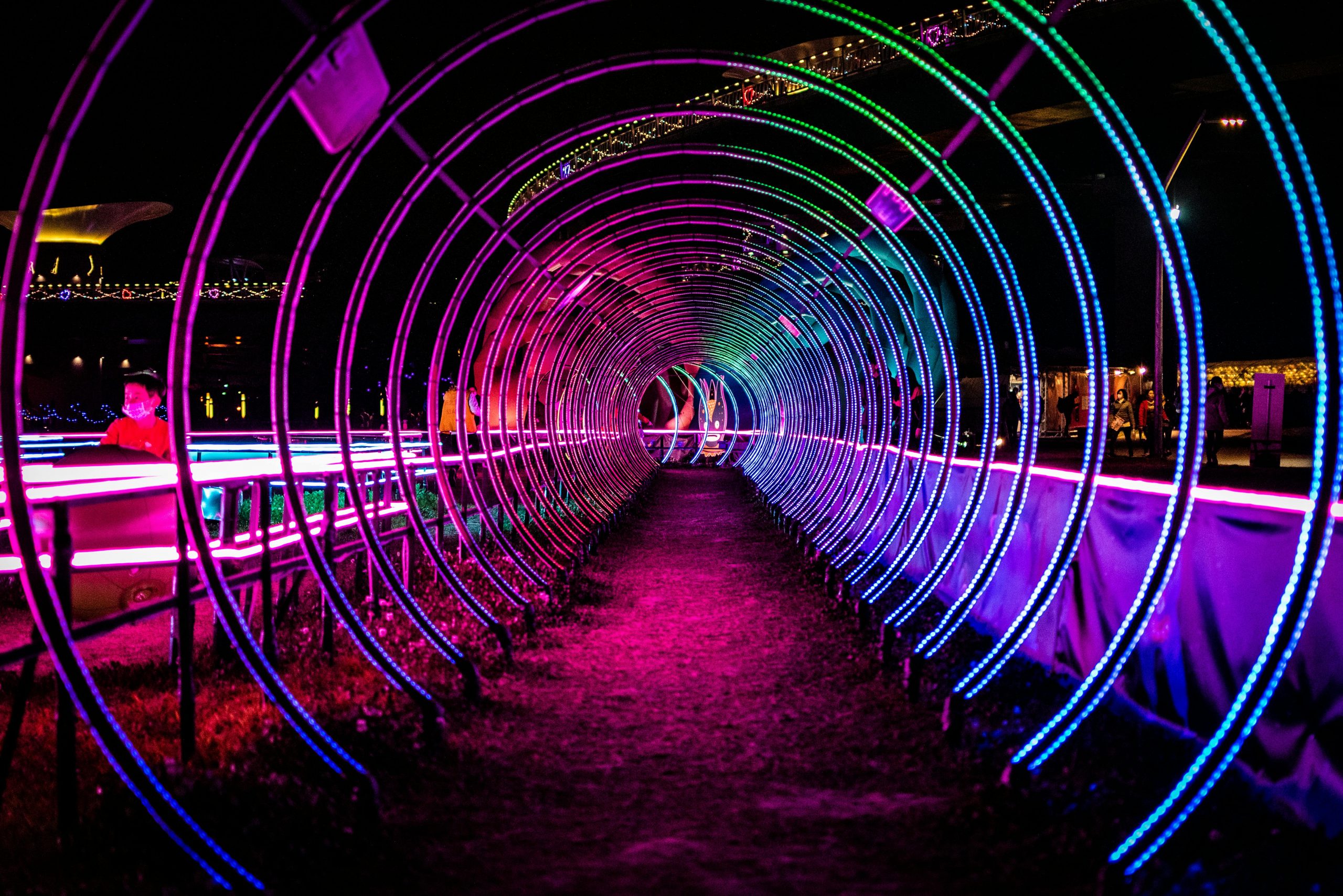 Colorful neon light tunnel creating a mesmerizing visual effect in a park at night.
