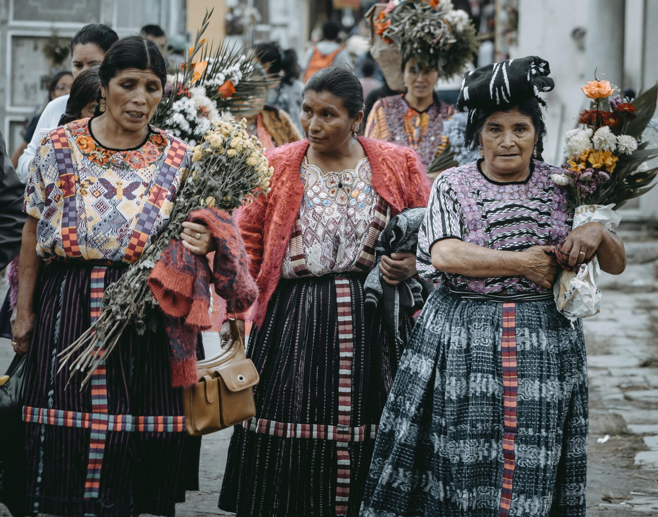 Women in traditional Guatemalan clothing gather with flowers, celebrating a cultural festival.
