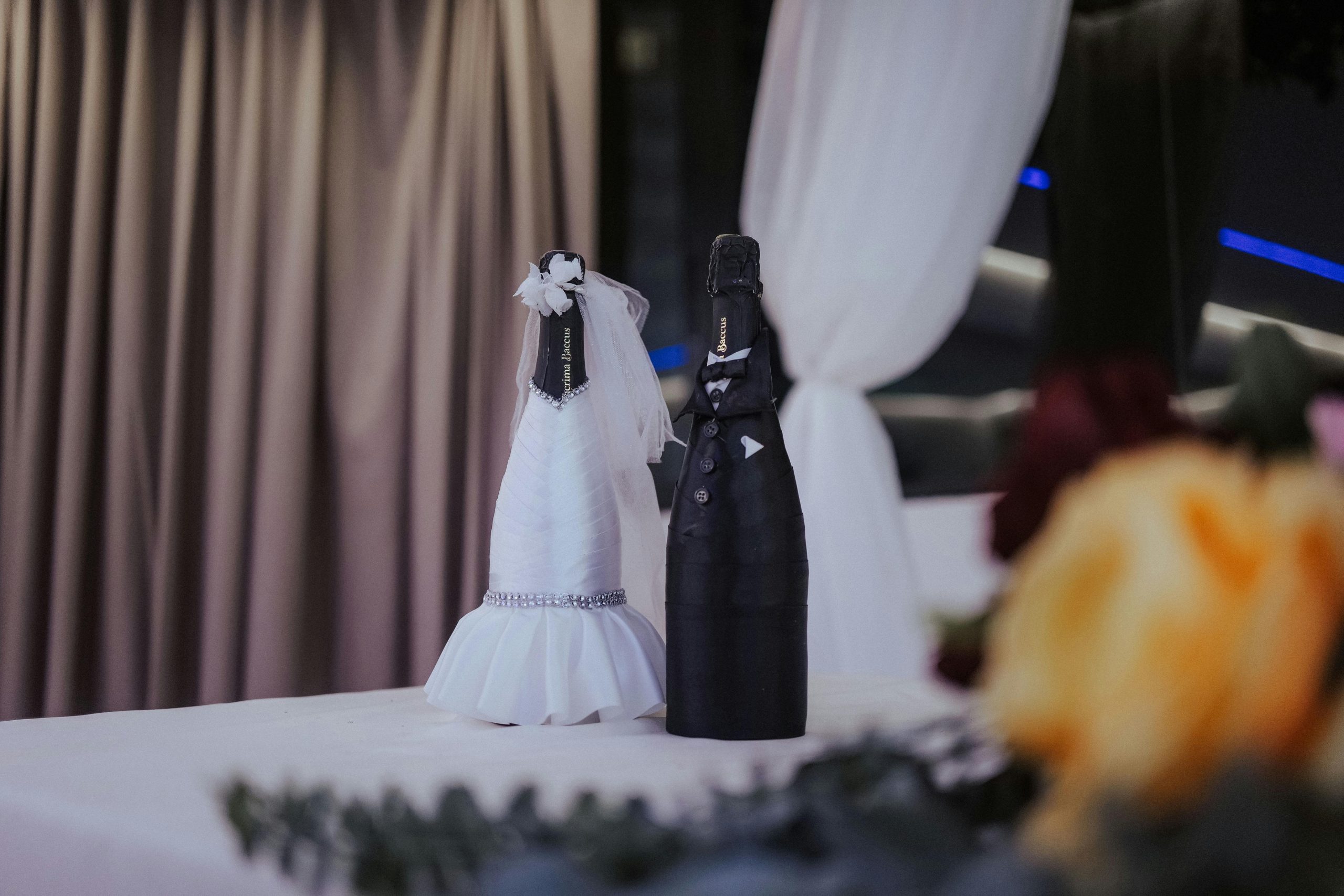 Champagne bottles dressed as bride and groom set on a decorated wedding table.