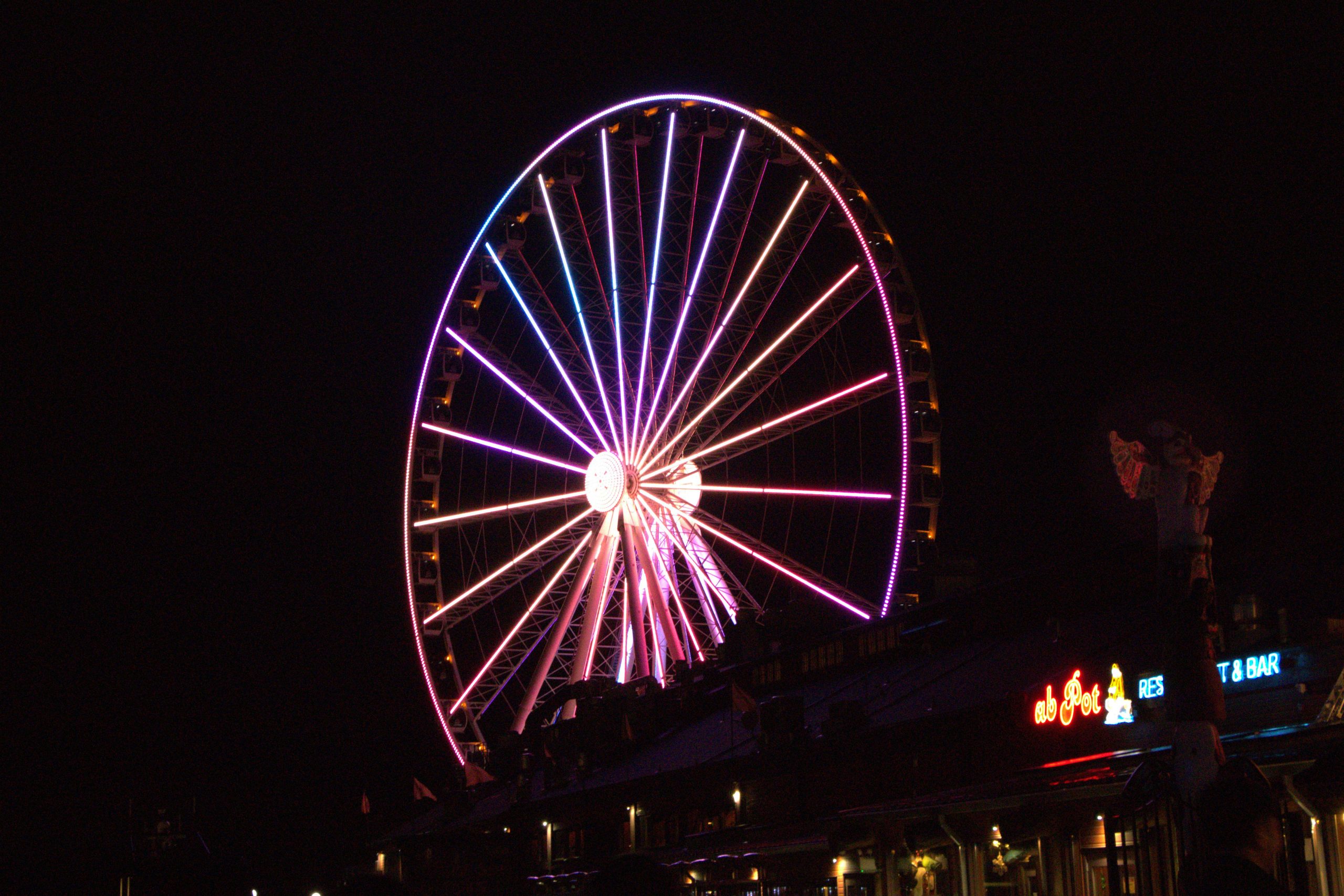Colorful neon lights on the Seattle Great Wheel pier during nighttime.