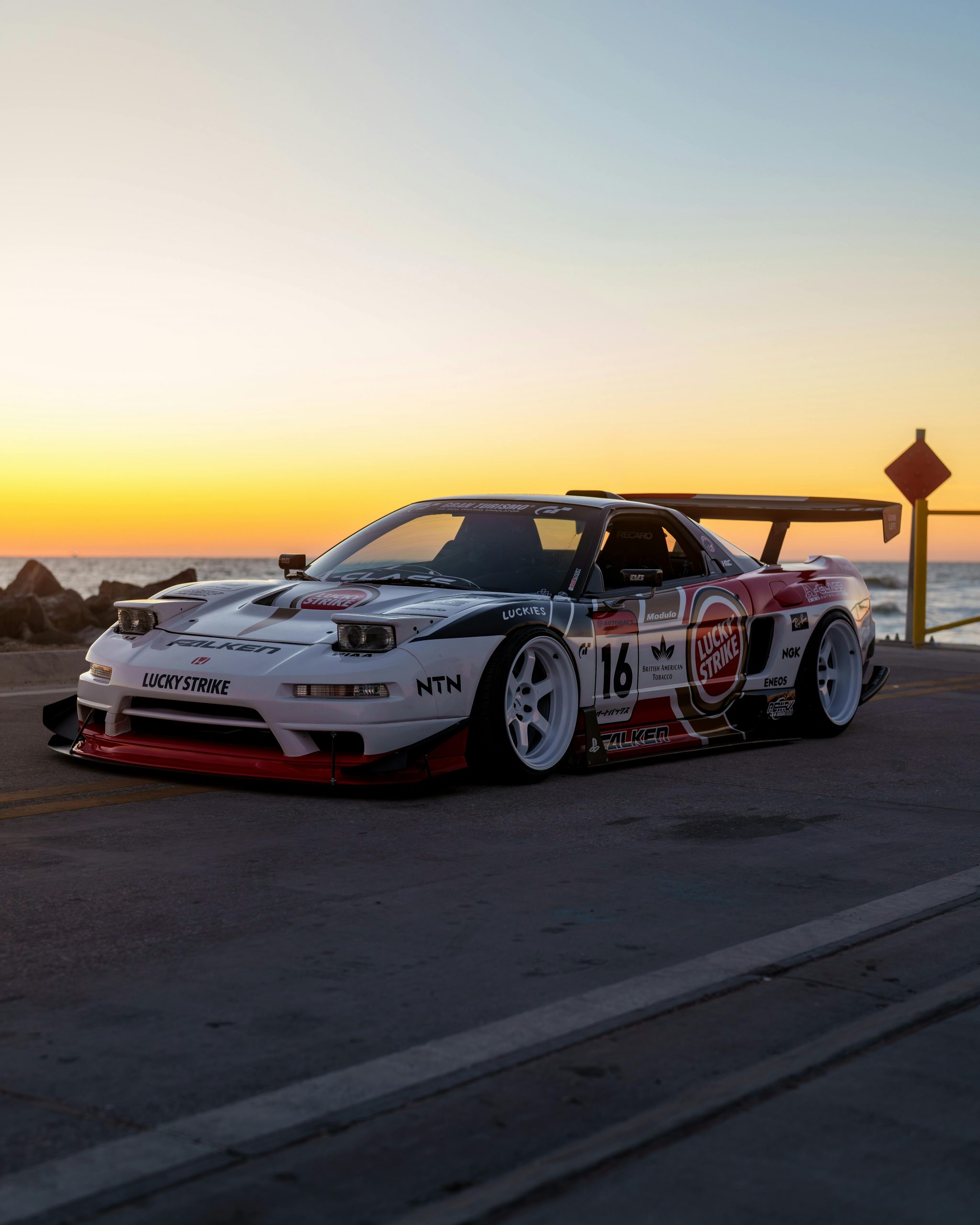 Sports car parked on coastal road at sunset, vibrant colors.