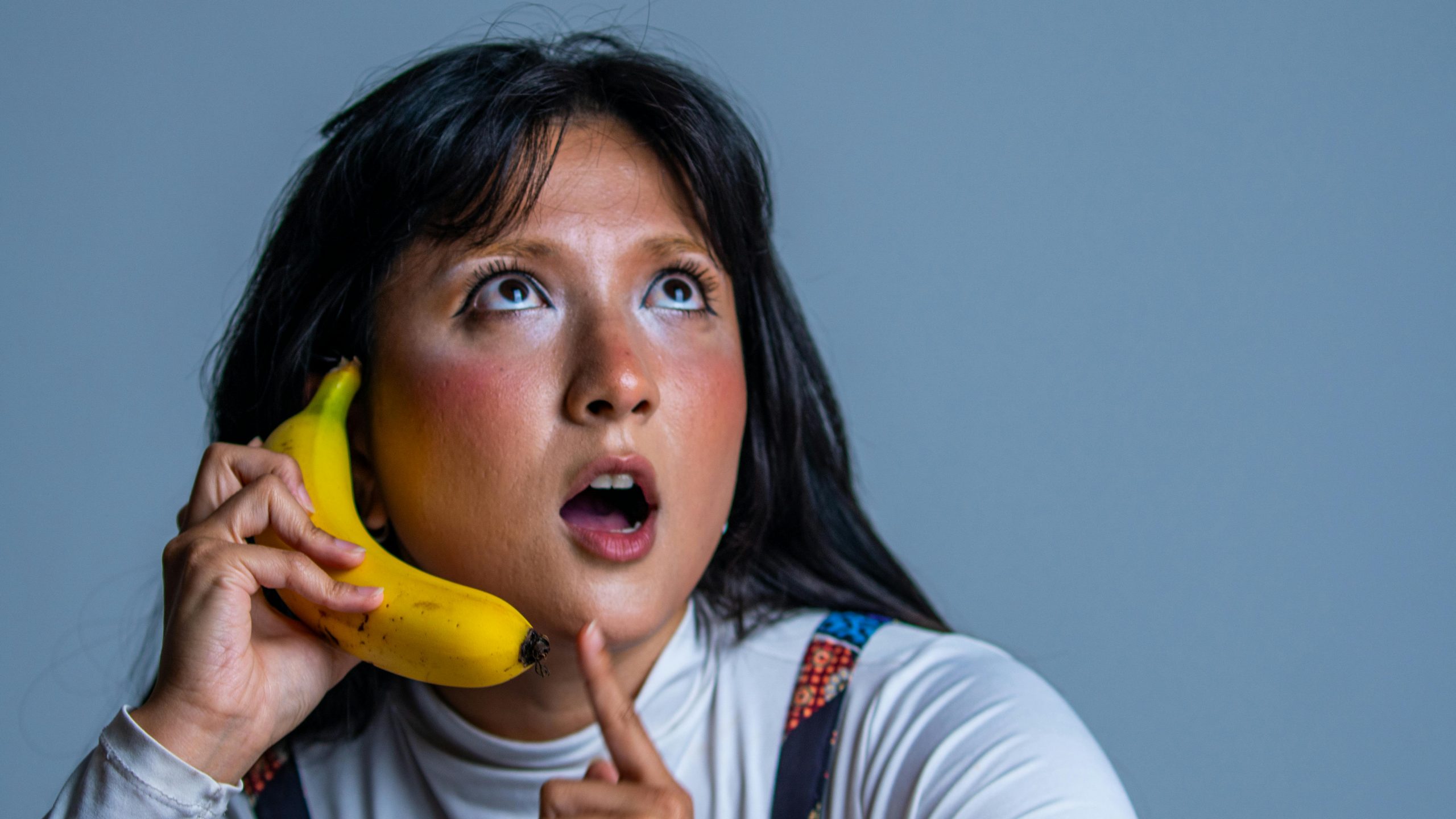 A thoughtful woman creatively uses a banana as a phone, expressing surprise.