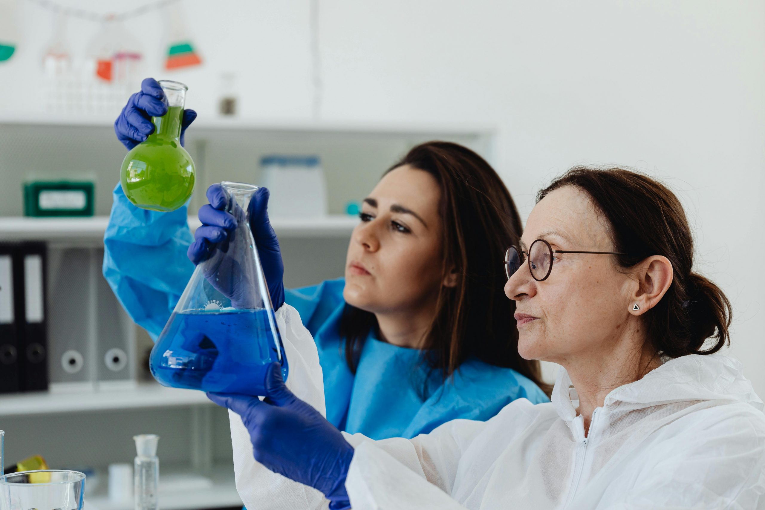 Two female scientists examine colored liquids in a lab setting, showcasing scientific research.