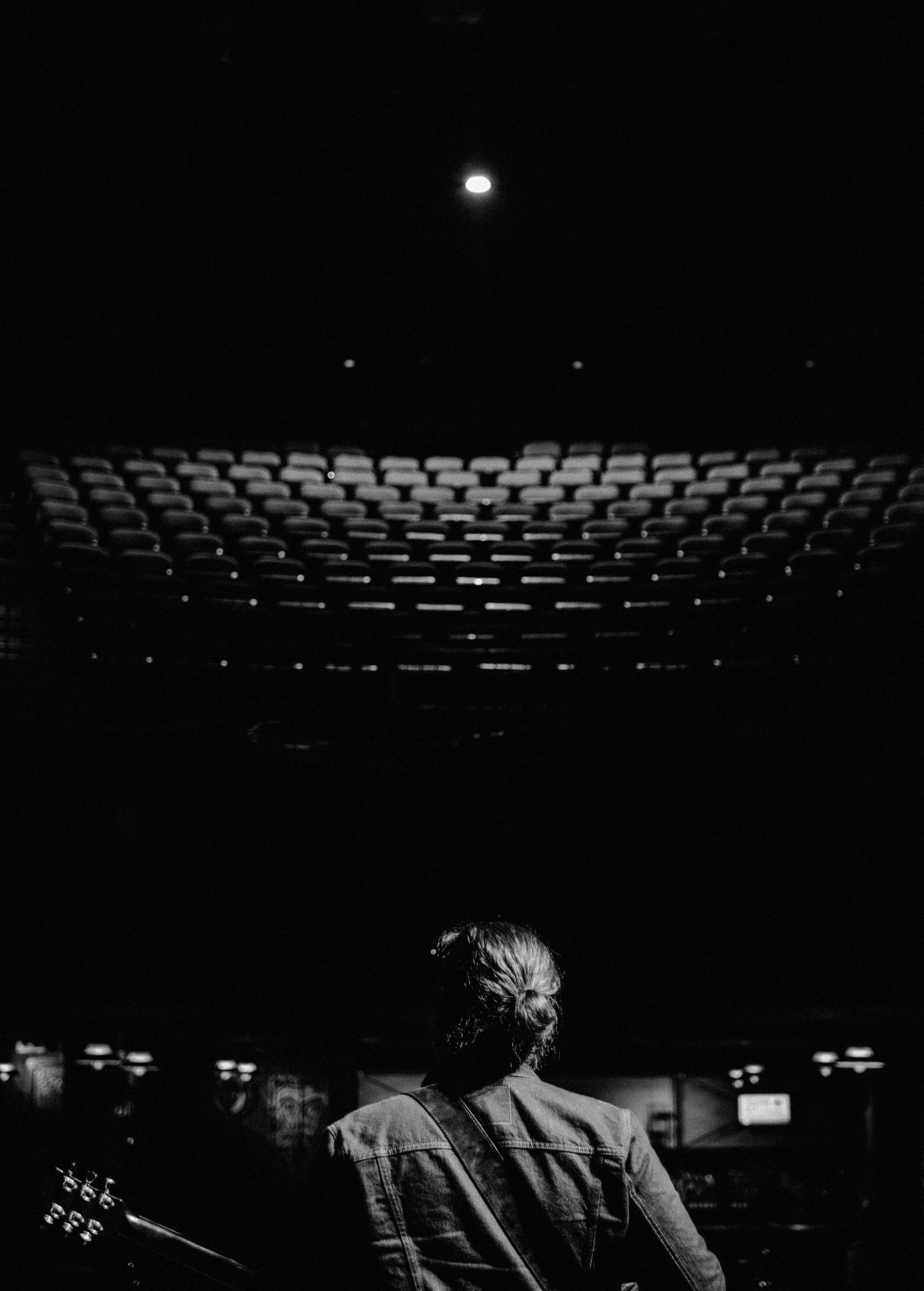 Black and white photo of a guitarist performing in an empty theater with spotlight.