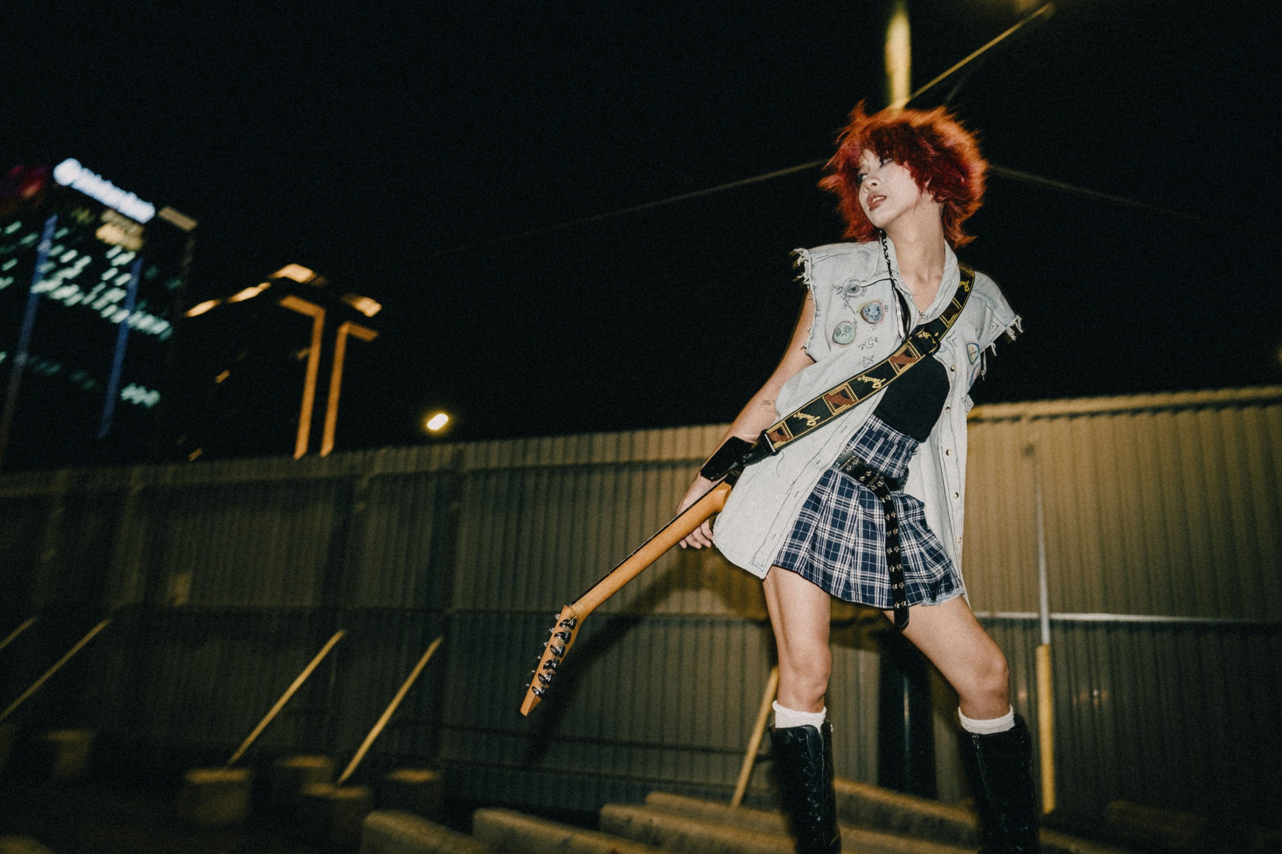 Young woman with electric guitar performing at night, embodying rock spirit with dyed hair and edgy style.