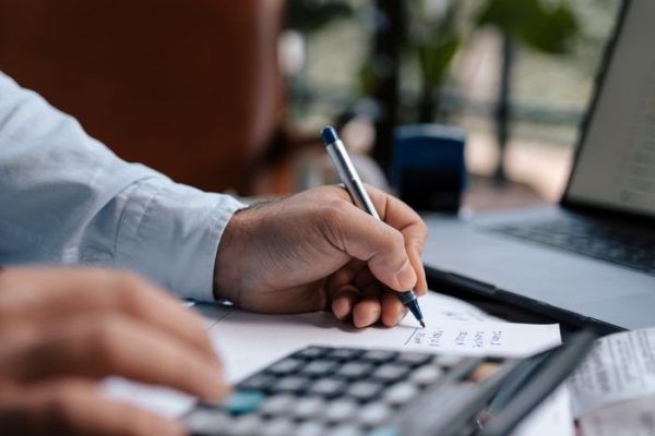 A person calculating finances with a calculator and pen on a desk indoors.